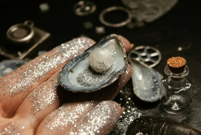 Una mano con brillantini e glitter mostra un'ostrica con la sua perla | Accademia delle Arti Orafe